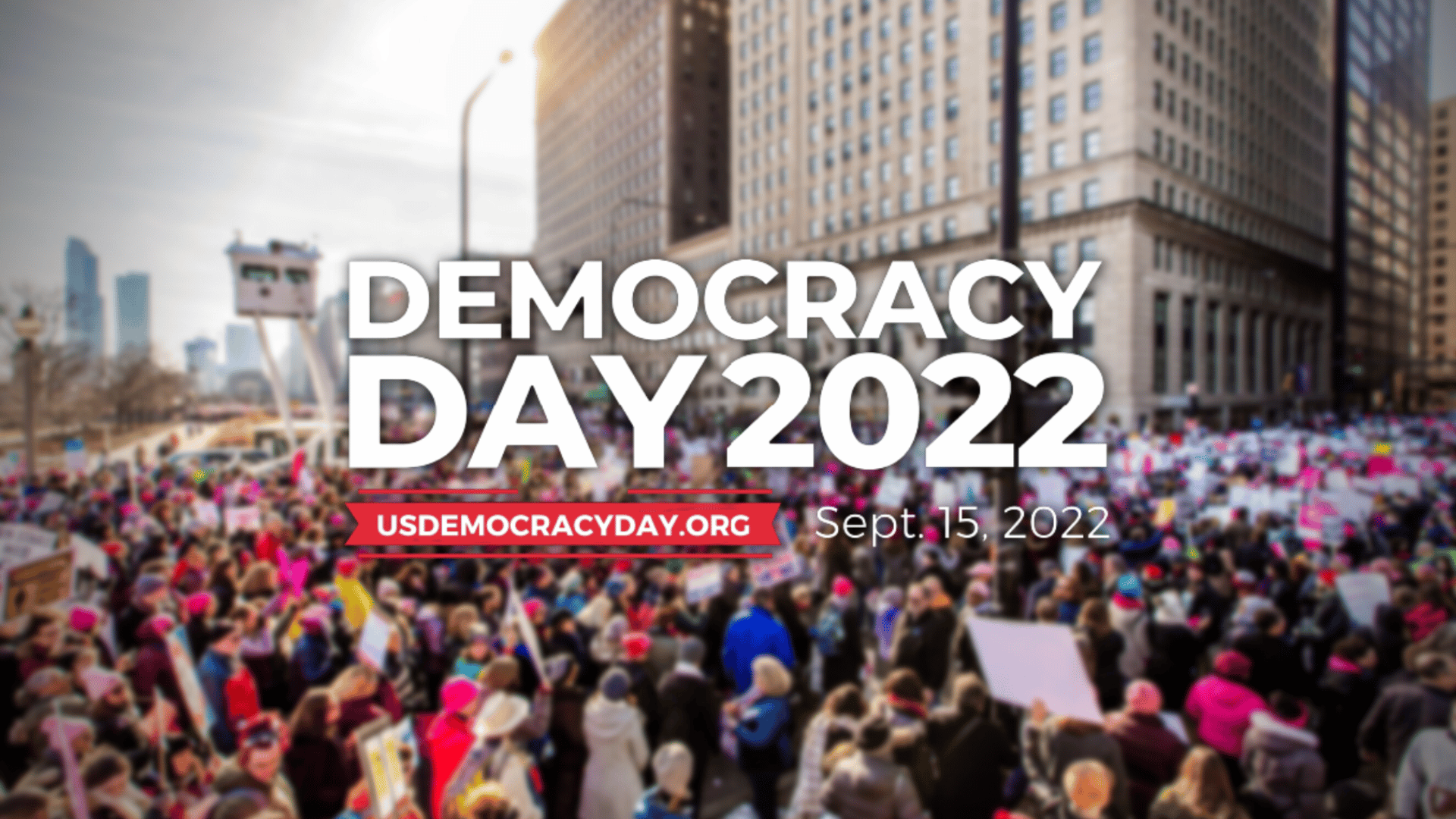 A crowd of demonstrators gathers in the streets in the background of the image, with the Democracy Day 2022 logo in the foreground.